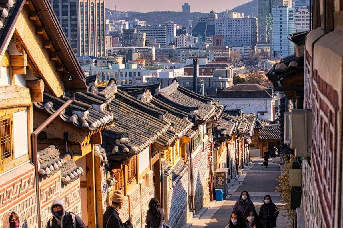 Traditional hanok tiled roofs lining an alley in Bukchon, with the Seoul skyline behind.